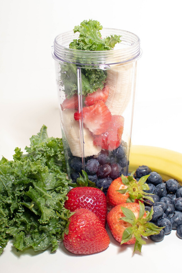Blender filled with blueberries banana strawberries kale