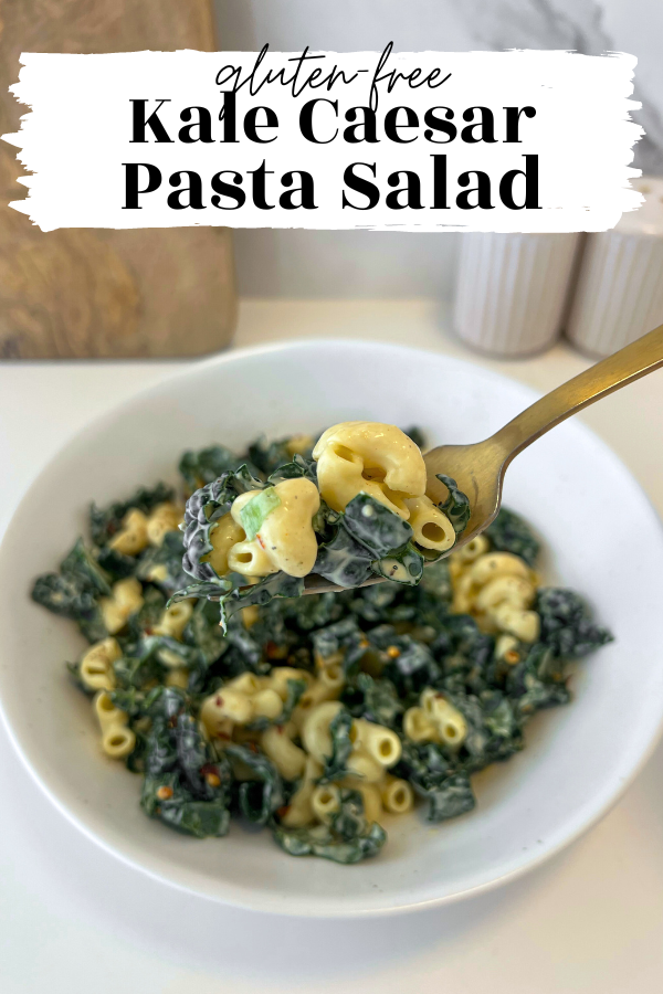 Close up of fork holding pasta and kale with bowl of caesar pasta salad in the background