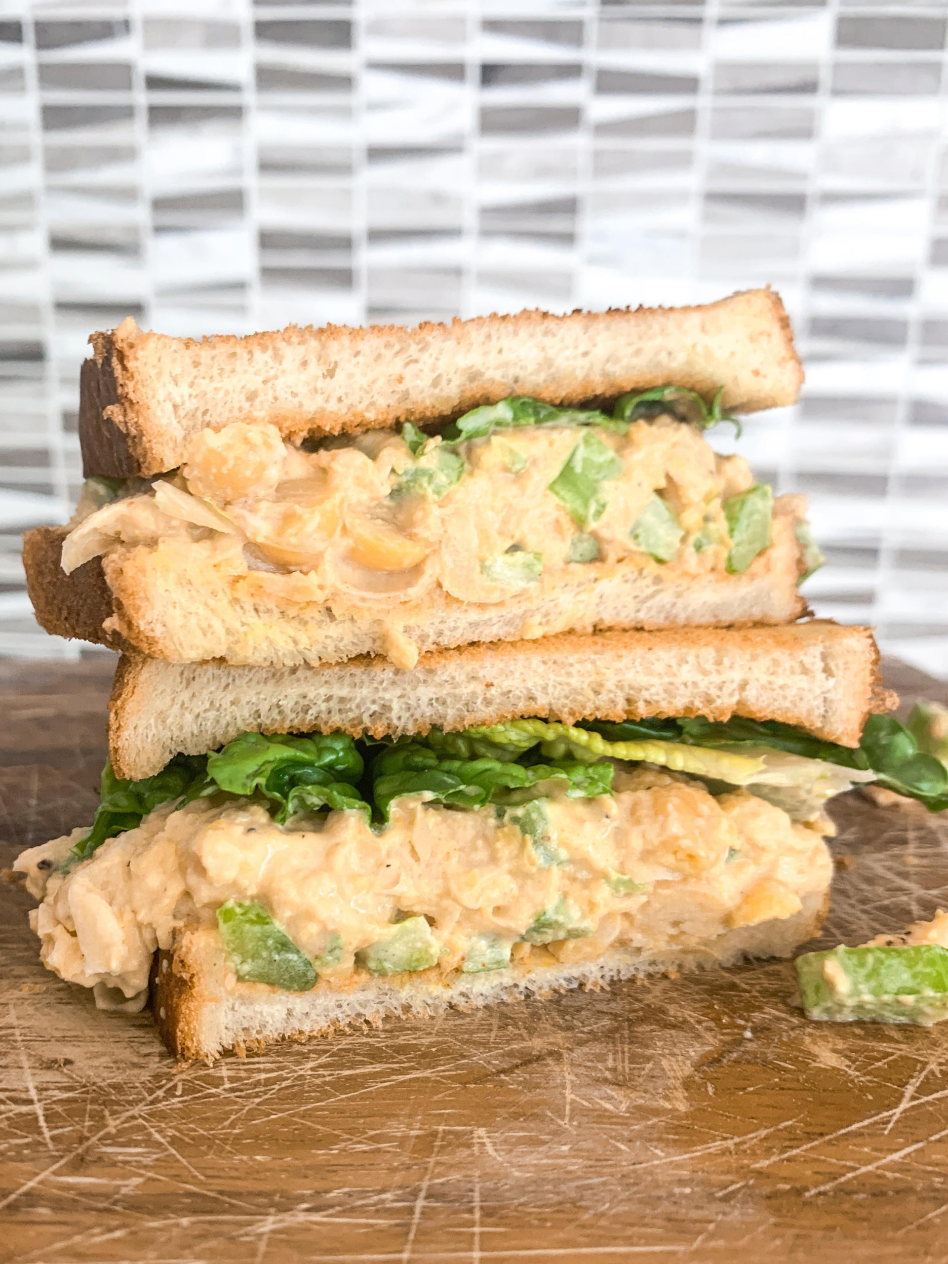 stacked chickpea salad sandwich in kitchen on wood cutting board