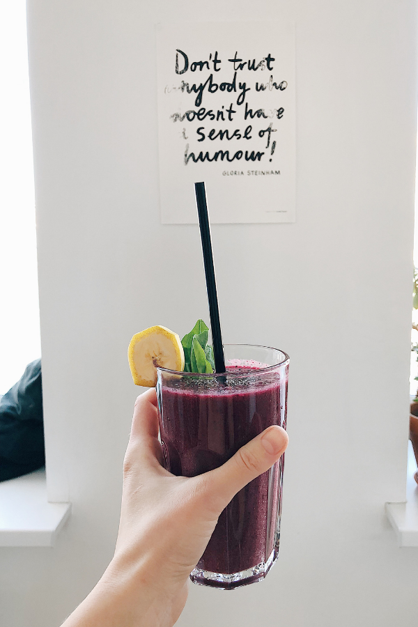 holding up a berry smoothie in front of a wall