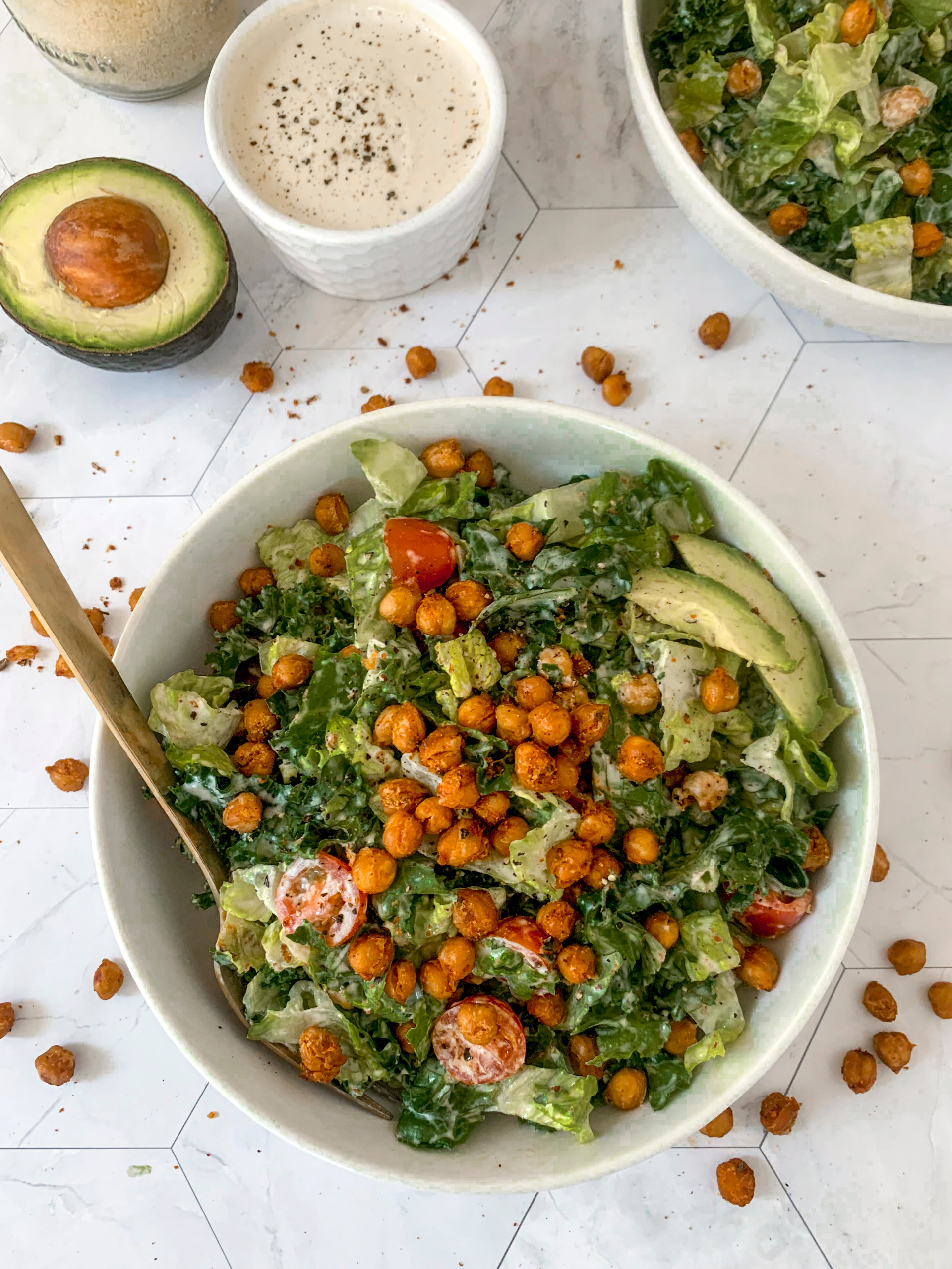 kale caesar salad with chickpeas, tomato and avocado in a white bowl 