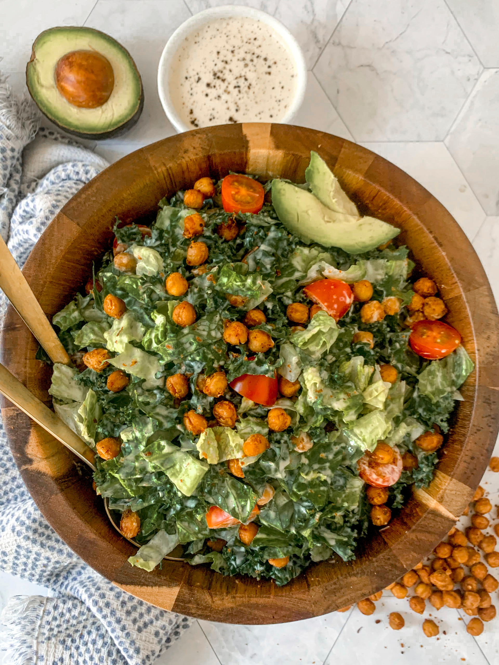 kale caesar salad in a wooden salad bowl with tomato, avocado, and chickpeas