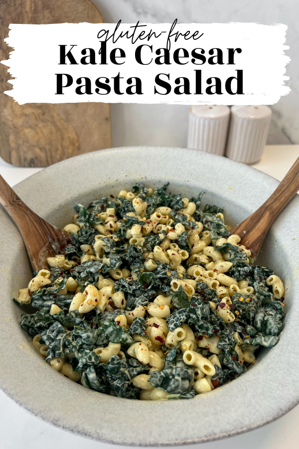 Large bowl of pasta salad with dino kale. Large wooden serving spoons sitting in bowl.